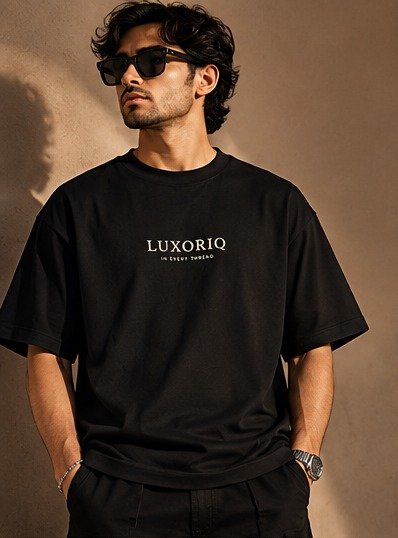 THE HOUSE TEE — INK — editorial front (model) Editorial lookbook mockup: model wearing the black THE HOUSE TEE — INK, front view with the small ivory LUXORIQ wordmark and IN EVERY THREAD on the chest
